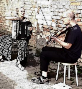 Georgia Huber und István Galus sitzen mit ihren Instrumenten auf Hockern vor einer Mauer