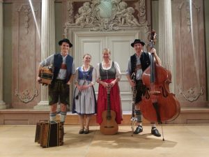 zwei Musikerinnen und zwei Musiker stehen in Bayerischer Trackt vor einer weißen Tür